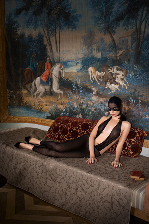 Žena v černém kostýmu s maskou na tváři sedí na pohovce