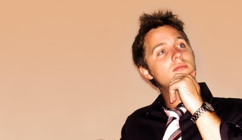 Fotografie muže, který je v černé košili s kravatou a má opřenou ruku o bradu