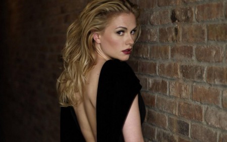 Blondýna stojící u zdi ukazuje záda