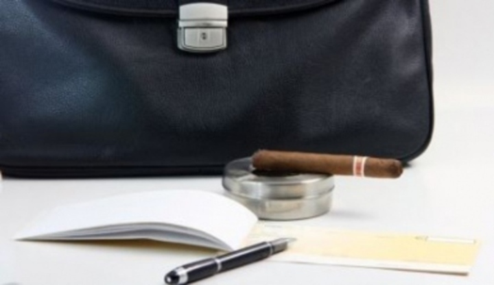 Fotografie zachycující pánskou tašku, doutník a diář s propiskou na stole