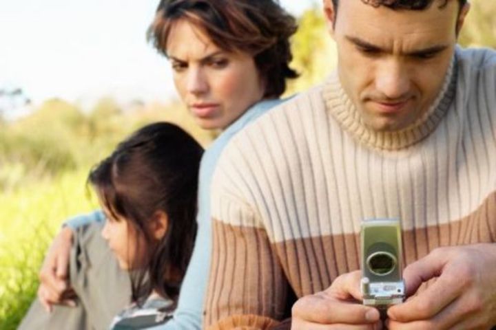 Žena nahlížející muži s telefonem v ruce přes rameno