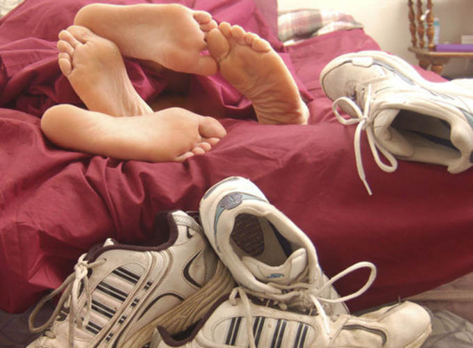 Sexuální mýty a omyly Fotografie páru, který leží na červeném prostěradle a před posteli jsou pohozeny tenisky