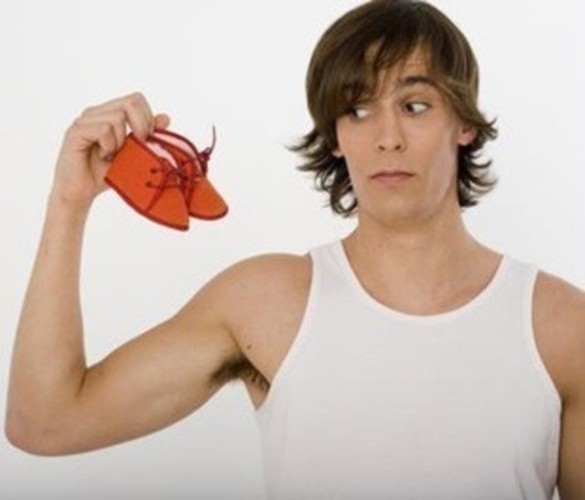 Fotografie muže v bílém tílku držící červené dětské botičky v ruce