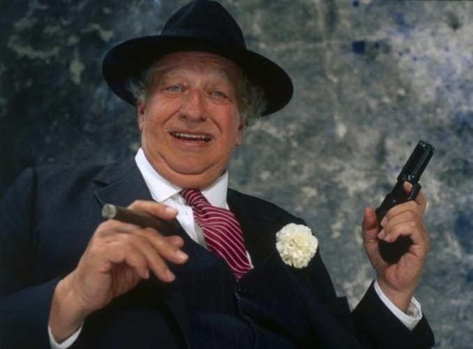 Snímek zachycující muže v obleku s doutníkem a se zbraní