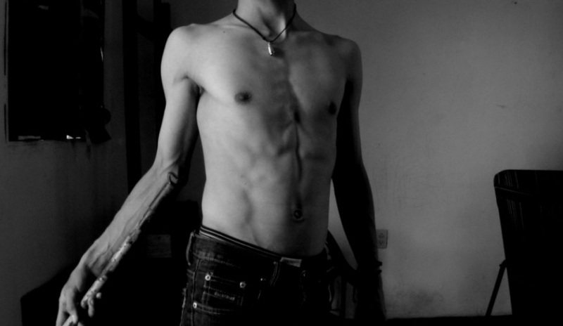 Černobílá fotografie muže v kalhotech s odhalenou hrudí