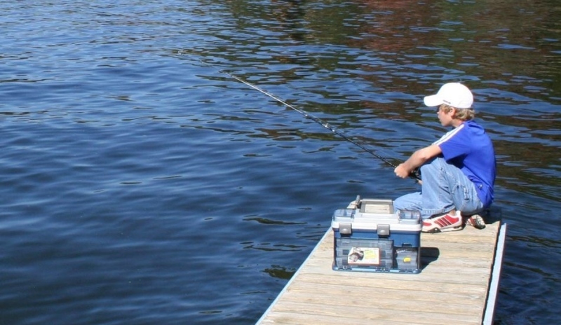 Snímek chlapce sedícího na molu s prutem v ruce