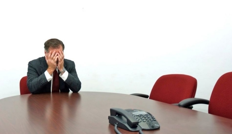 Fotografie muže sedícího u stolu s hlavou v dlaních s dvěma červenými židlemi a telefonem na stole