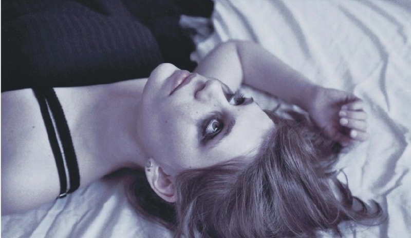 Fotografie ženy ležící na posteli s očima upřenýma vzhůru