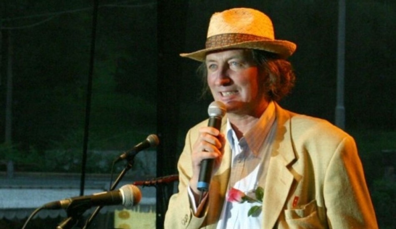 Muž s kloboukem na hlavě a mikrofonem v ruce