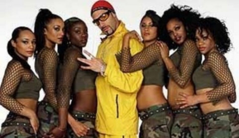 Fotografie muže ve žlutém oblečení obklopeného šesti ženami