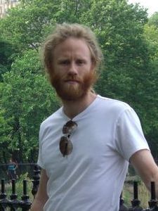 Vousatý muž v bílém triku stojící v přírodě