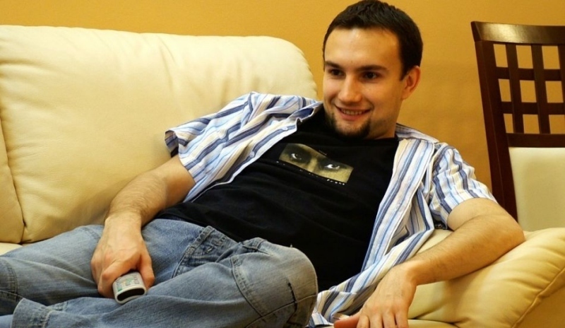 Fotografie muže sedícího na pohovce v džínách, černém triku a proužkované košili