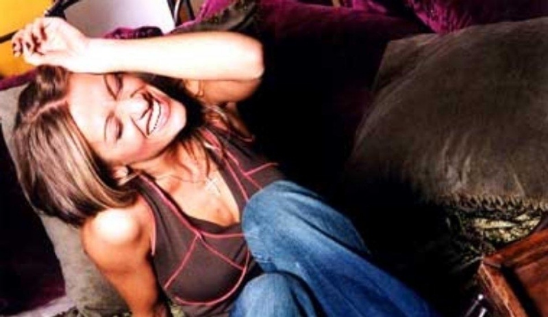 Dara Rolins sedící v kalhotech a triku s úsměvem na tváři