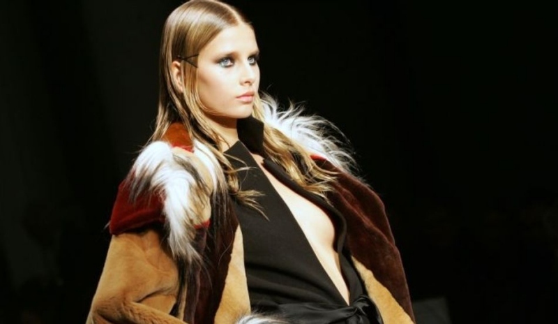 Fotografie ženy sedící v barevné bundě s kožešinou na černém pozadí