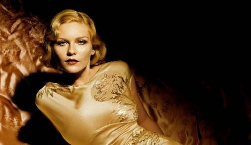 Kirsten Dunst ležící na posteli v dlouhých lesklých šatech