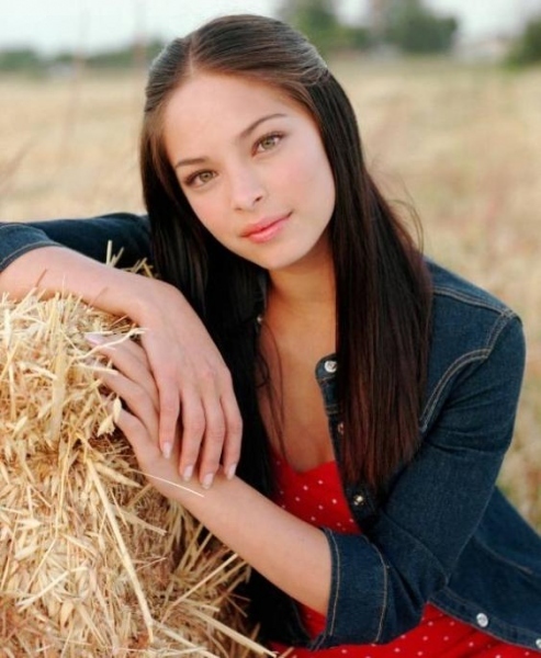 Kristin Kreuk se na poli opírá o balík slámy
