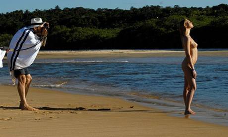 Muž fotící na břehu moře nahou ženu
