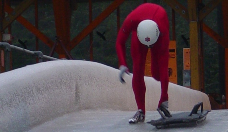 Fotografie muže v červené kombinéze a nízkou desku se dvěma držadly provozující Skeleton