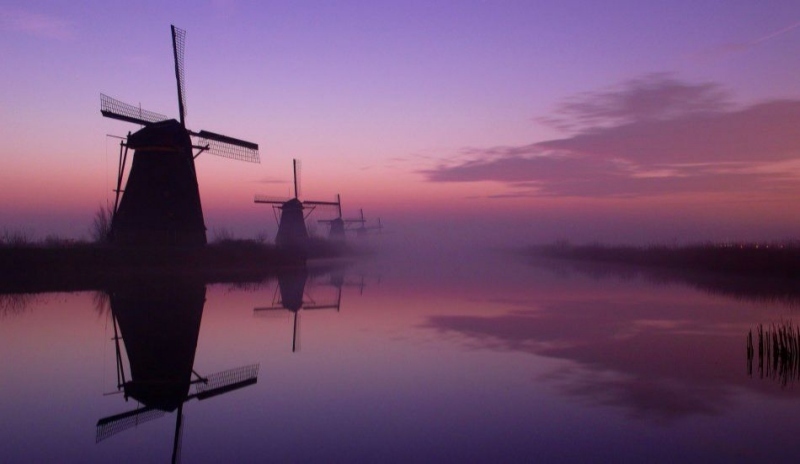 Větrné mlýny stojící v řadě za sebou u řeky