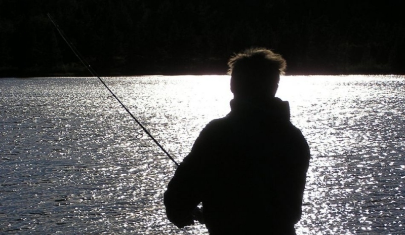 Rybář stojící s prutem u vody