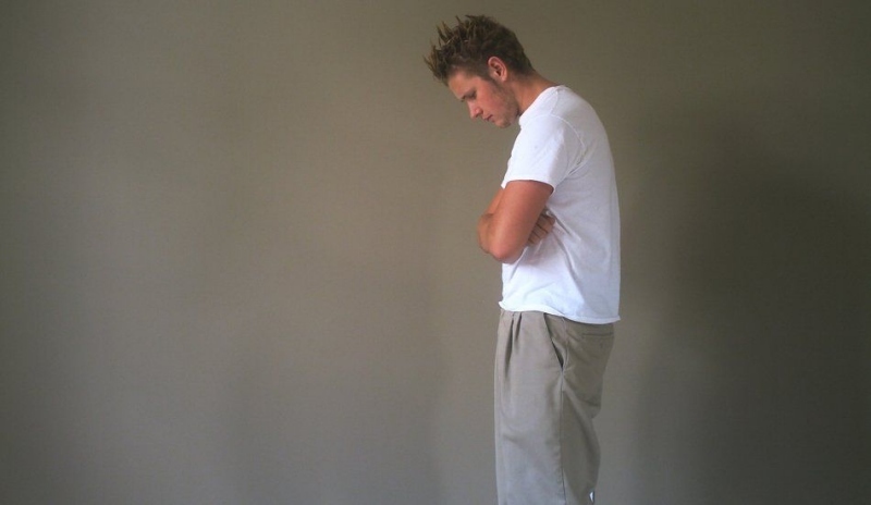 Fotografie muže se založenými rukami a s hlavou skloněnou dolů