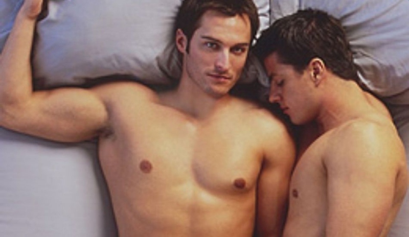 Fotografie dvou nahých mužů ležících v posteli