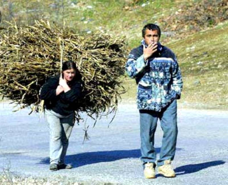 Muž kouřící cigaretu se ženou nesoucí břímě na zádech