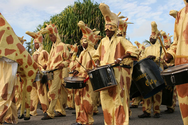 Průvod lidí v maskách žirafy s bubny