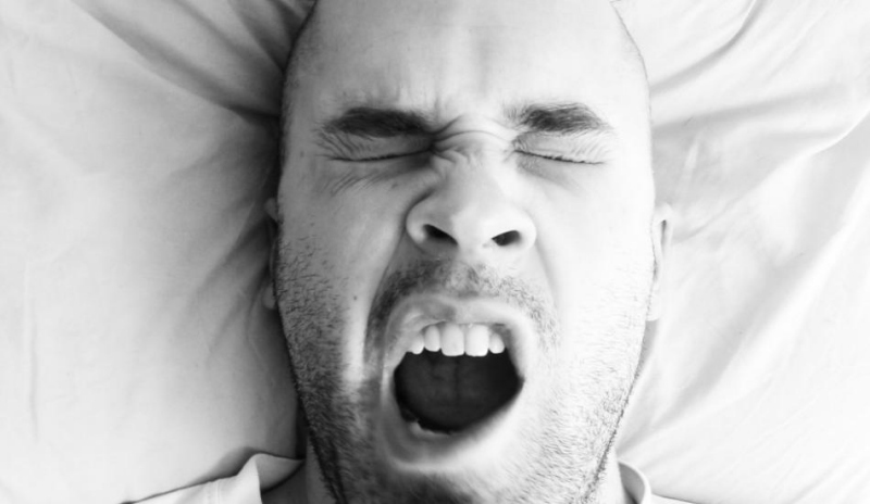Muž ležící v posteli na zádech a zívá